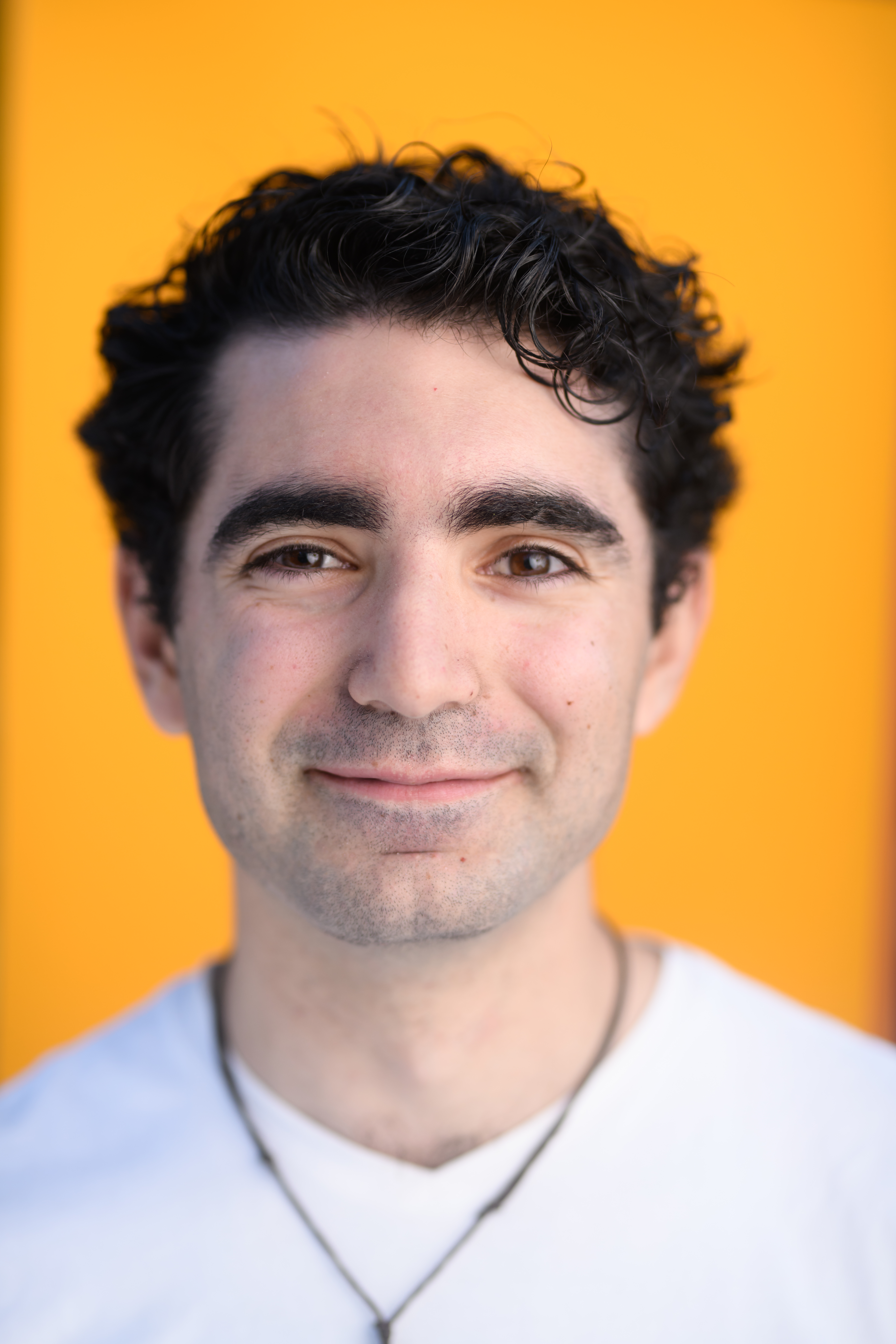 A professional photo of Matthew Blanco. He is smiling at the camera in front of a brick wall.